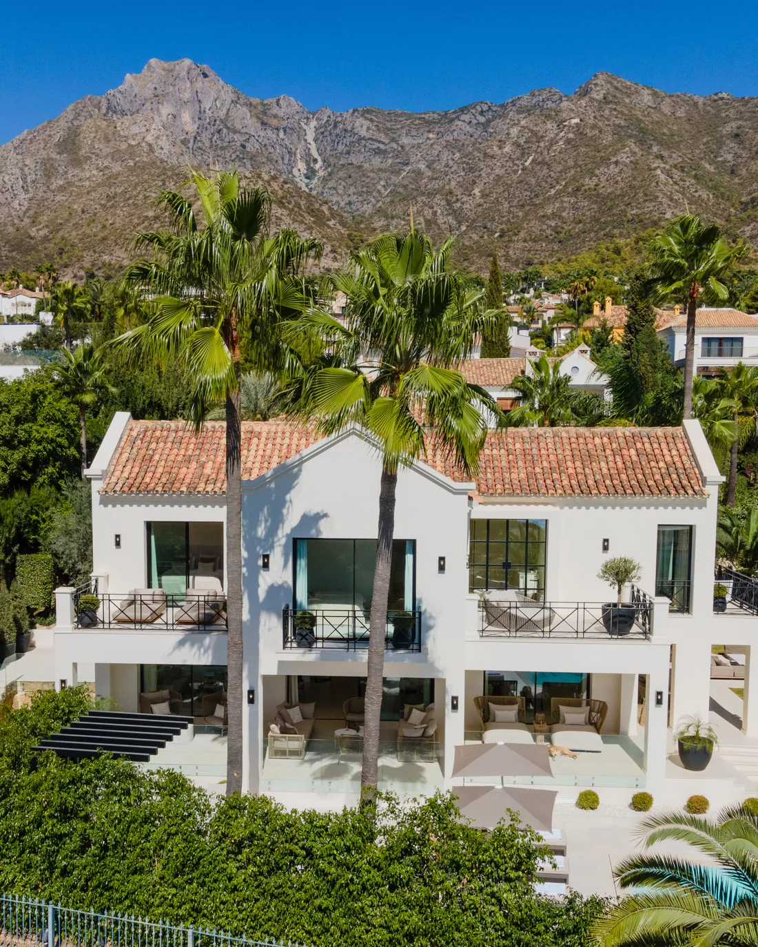 Vista aérea de una villa blanca con piscina y jardín con la sierra de Marbella al fondo
