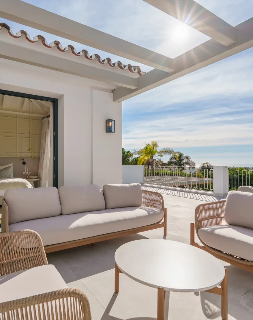Terraza con sofás exteriores y vistas a la costa bajo una pérgola