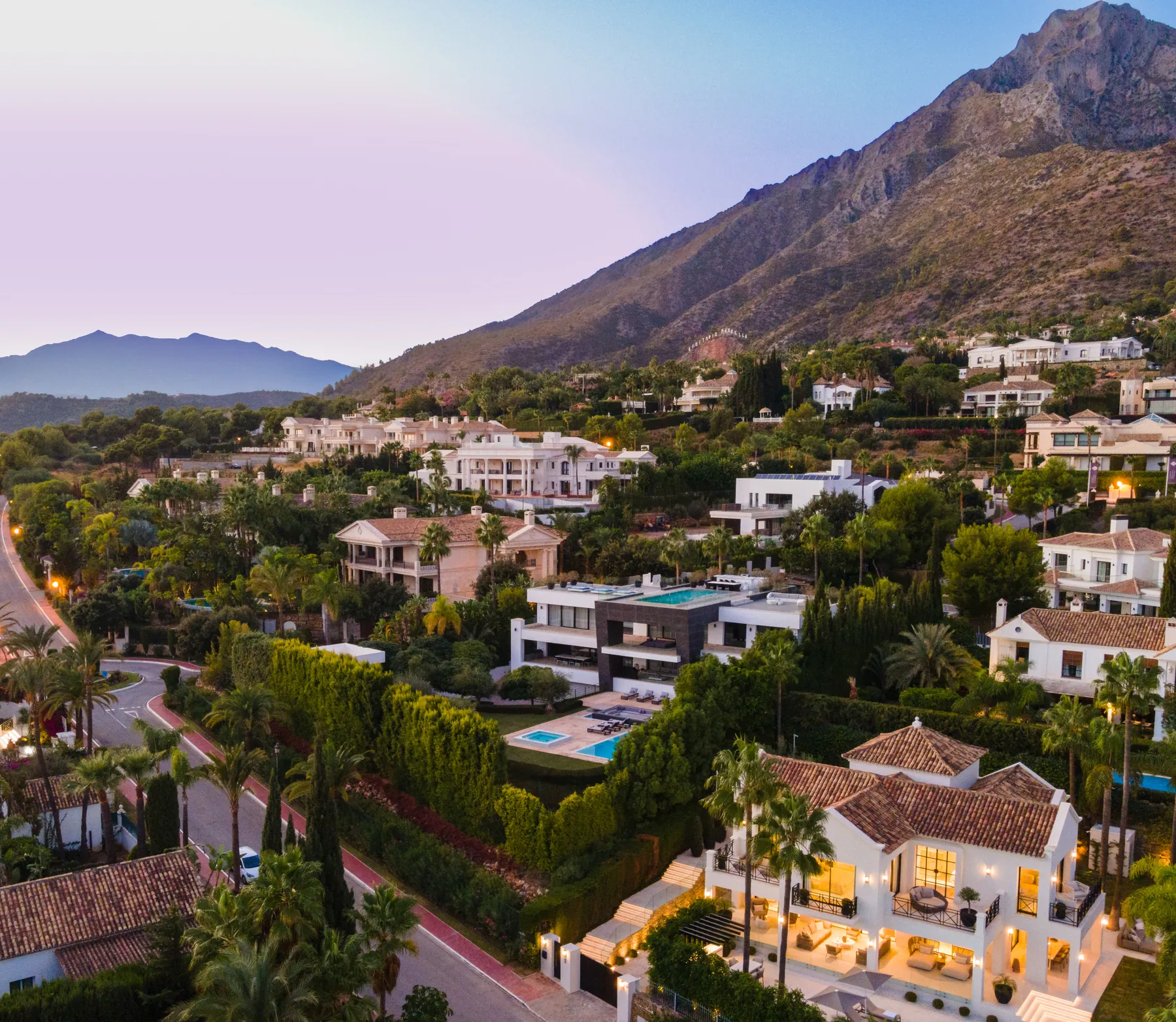 Vista aérea de villas de lujo iluminadas al anochecer bajo la sierra de Marbella