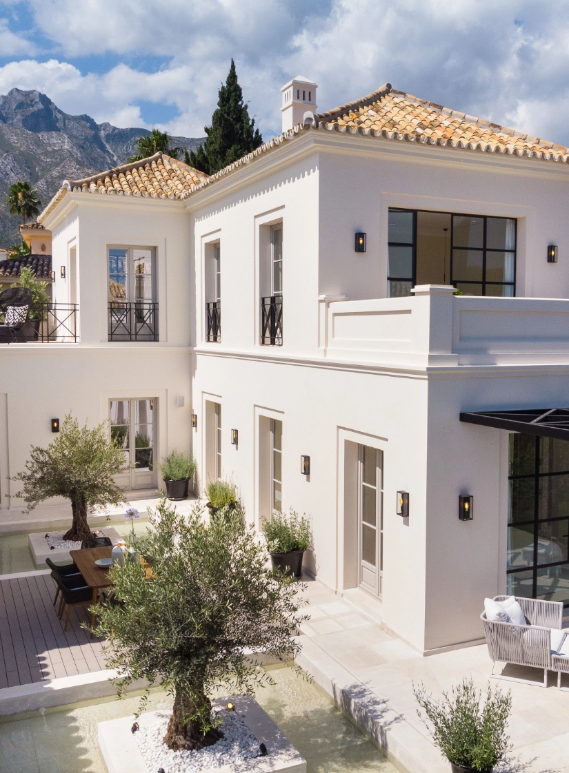 Mansión de inspiración andaluza con fachada blanca y patio con olivo