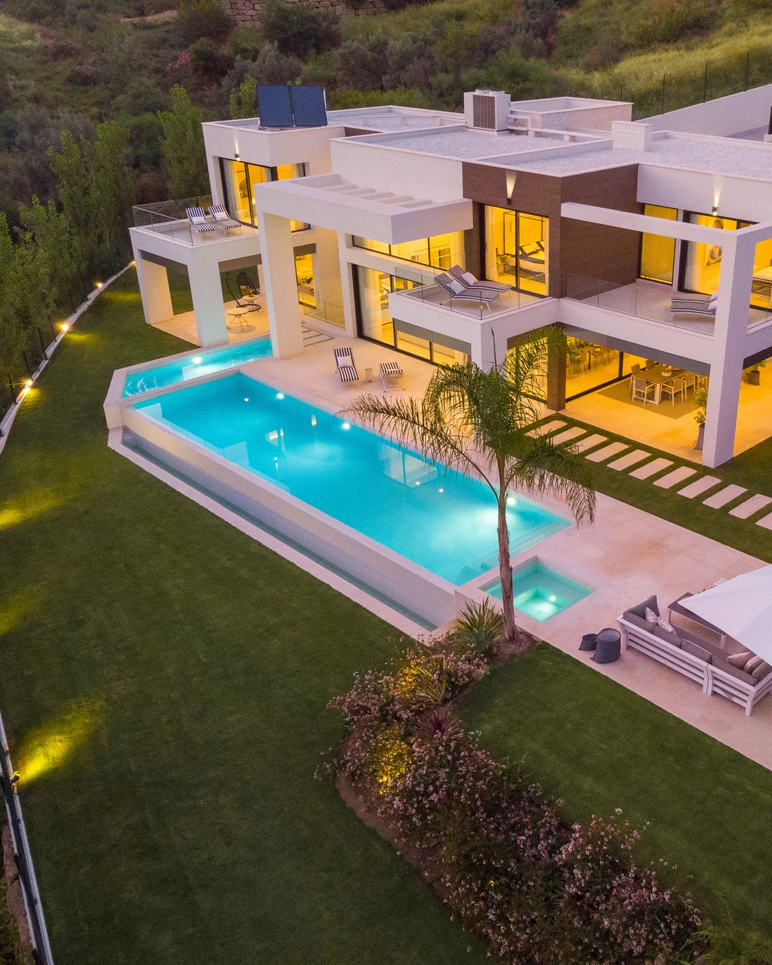 Aerial view of a contemporary villa with infinity pool and sloping garden at dusk