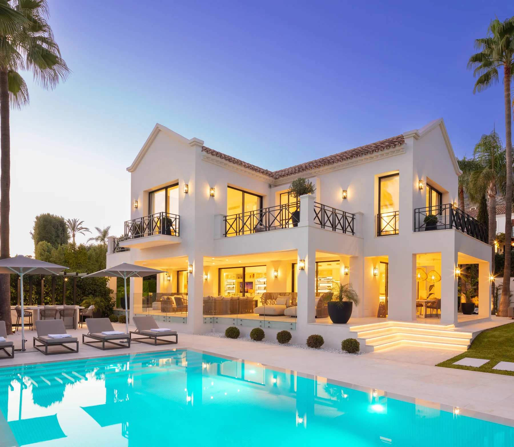 White Mediterranean villa lit up with pool and garden at dusk
