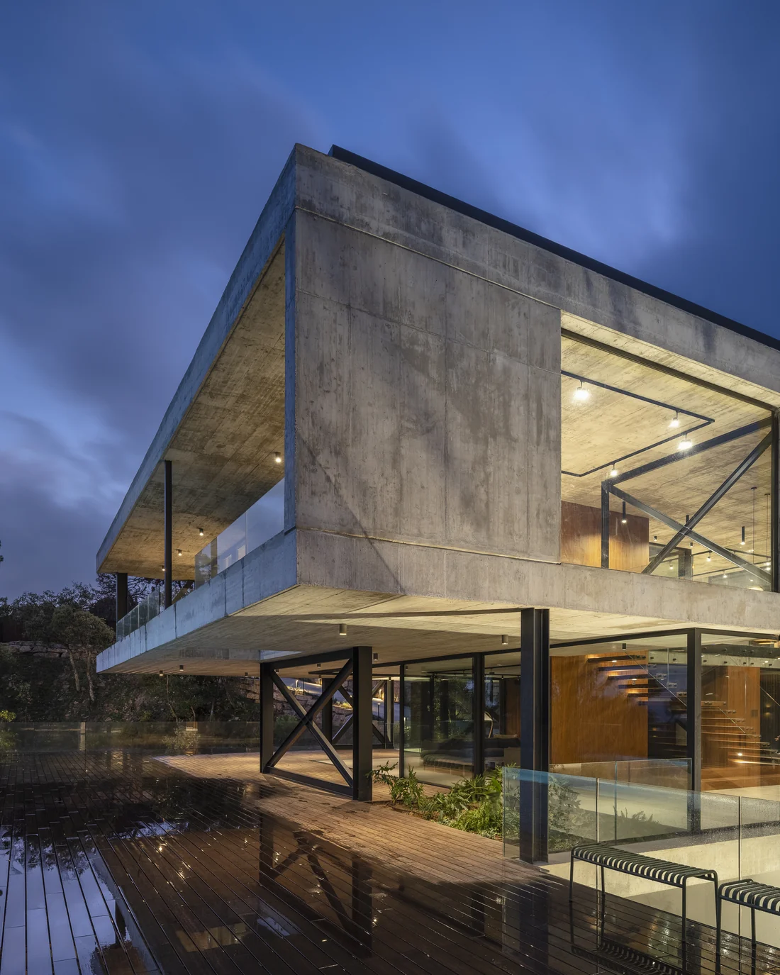 Exposed-concrete villa with a cantilevered volume and large glazed walls at dusk