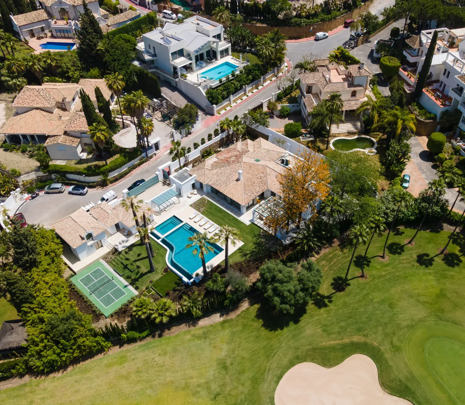 Vista aérea de una villa con piscina y pista de tenis junto al green de un campo de golf