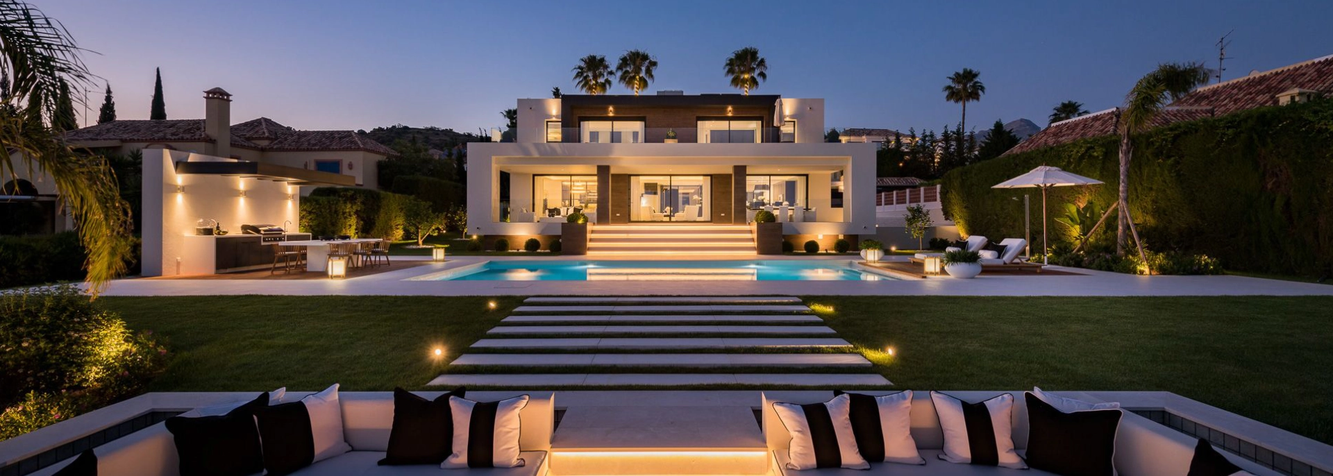 Villa at dusk with illuminated lawn steps and pool