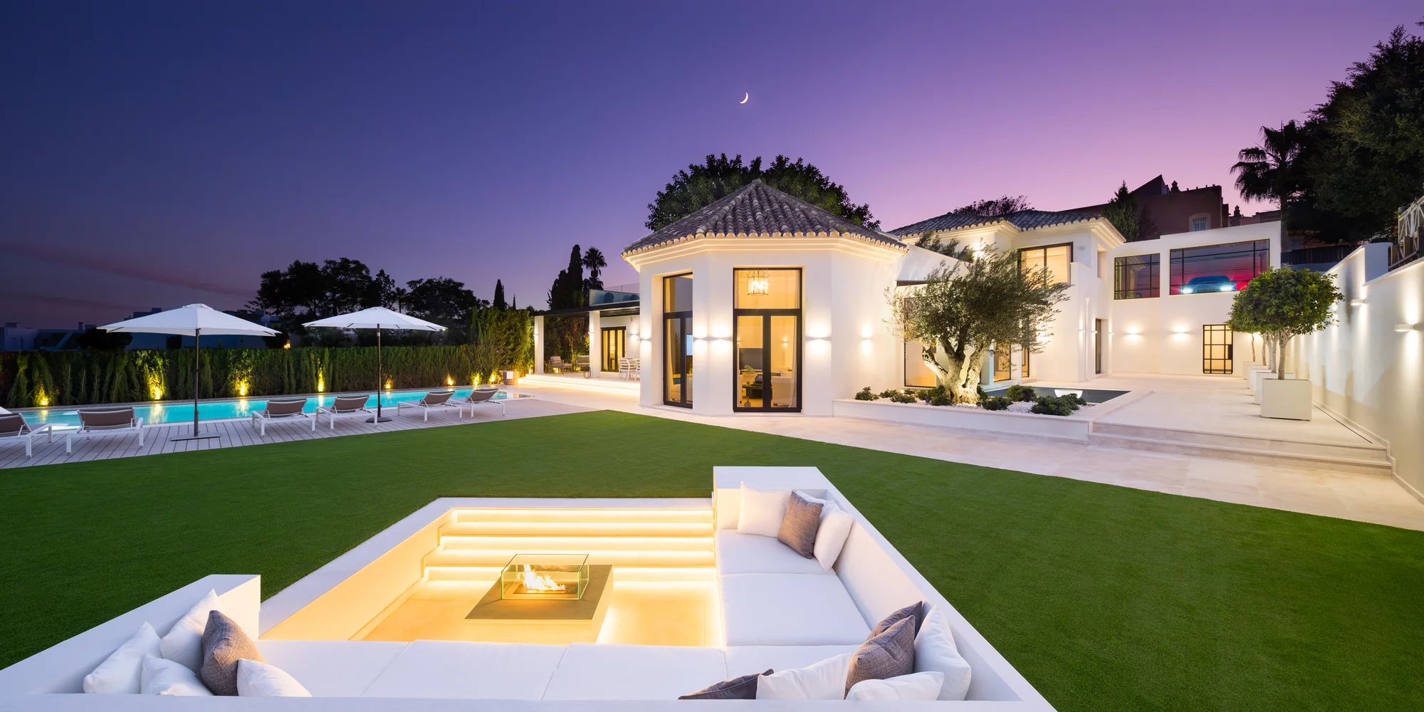 Villa Alaya en Marbella: jardín con salón exterior hundido y fachada iluminada al anochecer